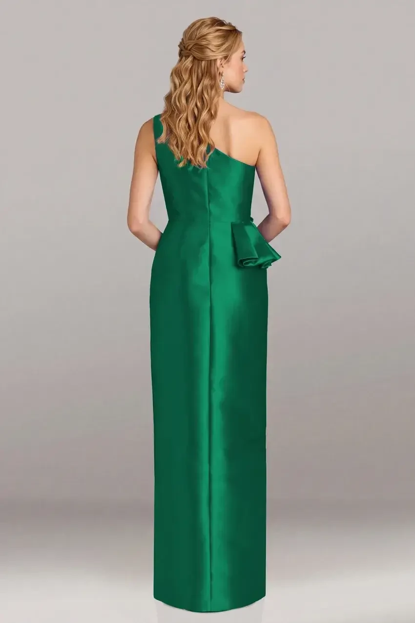 A woman wearing a one-shoulder green evening gown with a side bow and a thigh-high slit, standing against a neutral background.