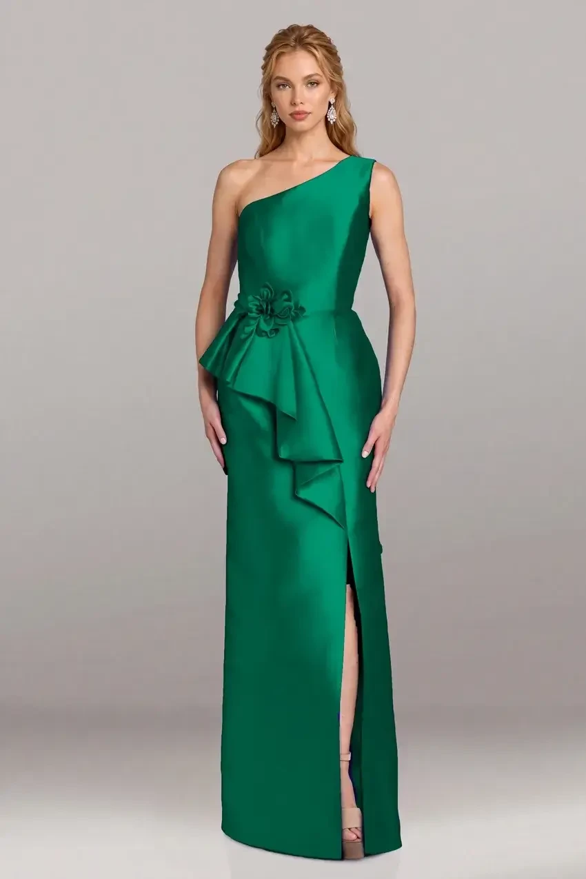 A woman wearing a one-shoulder green evening gown with a side bow and a thigh-high slit, standing against a neutral background.