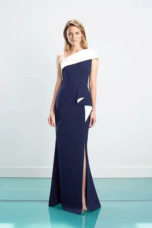 A woman in an elegant navy blue and white gown stands on a turquoise floor. The gown features an asymmetrical shoulder and a thigh-high slit, exuding sophistication.