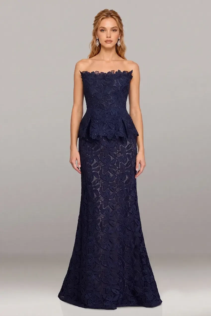 A woman wearing a strapless navy blue gown with a peplum waist and intricate lace details.
