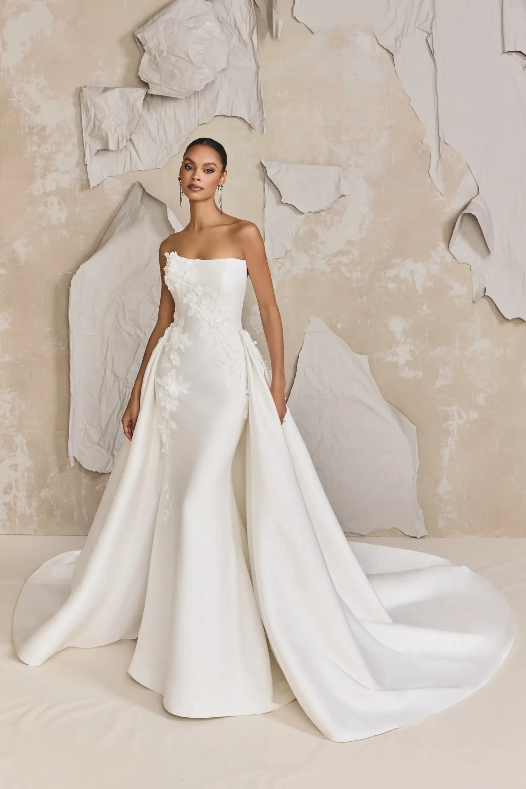 model is wearing a strapless fit and flare bridal gown with a detachable overskirt