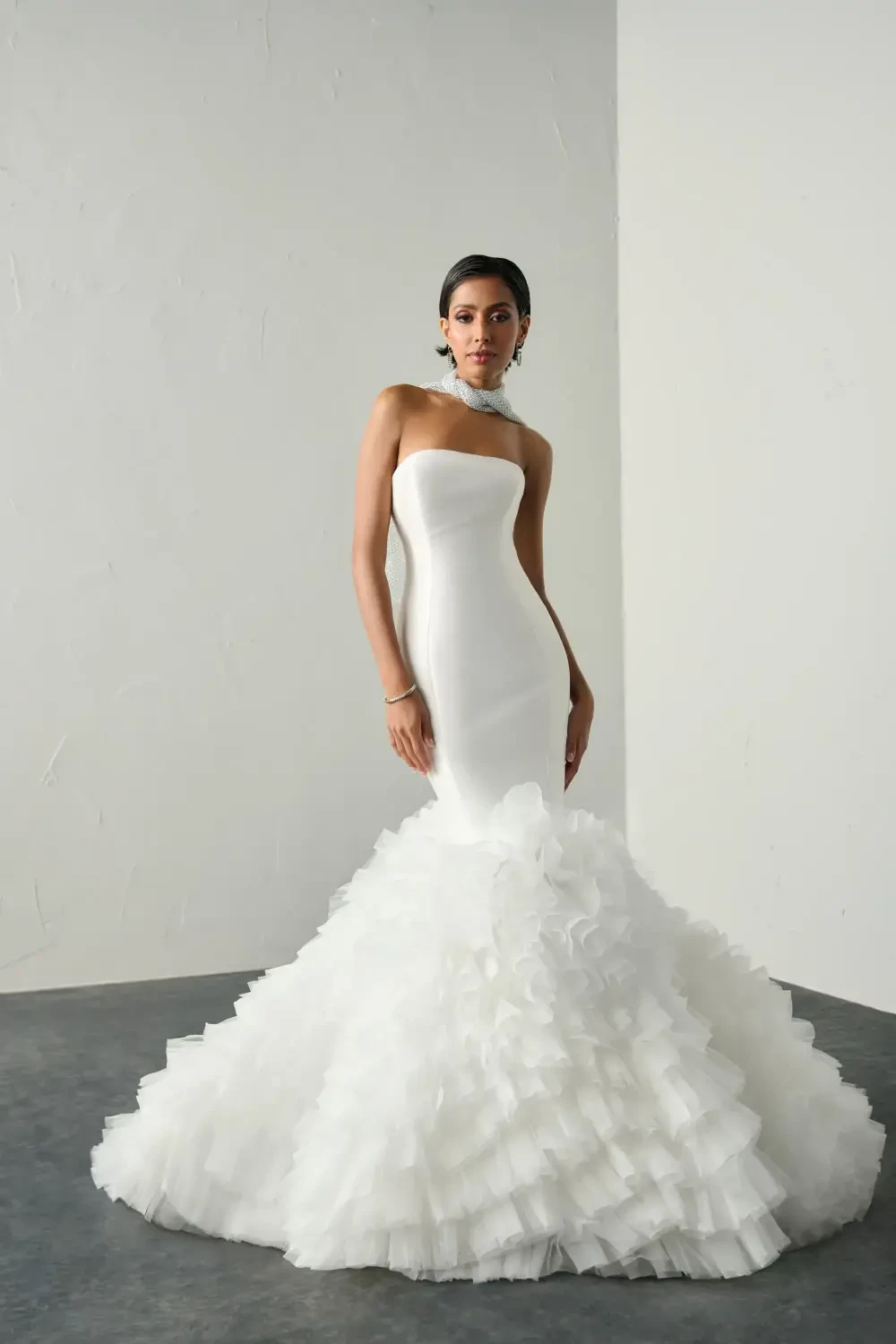 A woman wearing a strapless white dress with a ruffled bottom, posing elegantly.