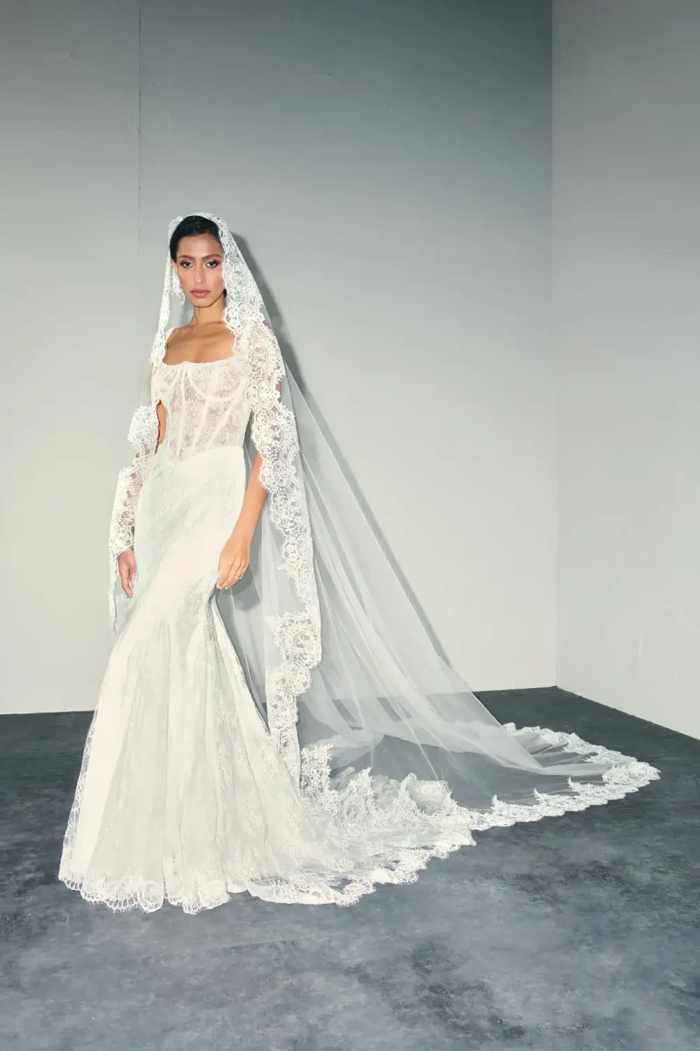 model is wearing a lace bridal gown with a dramatic lace veil
