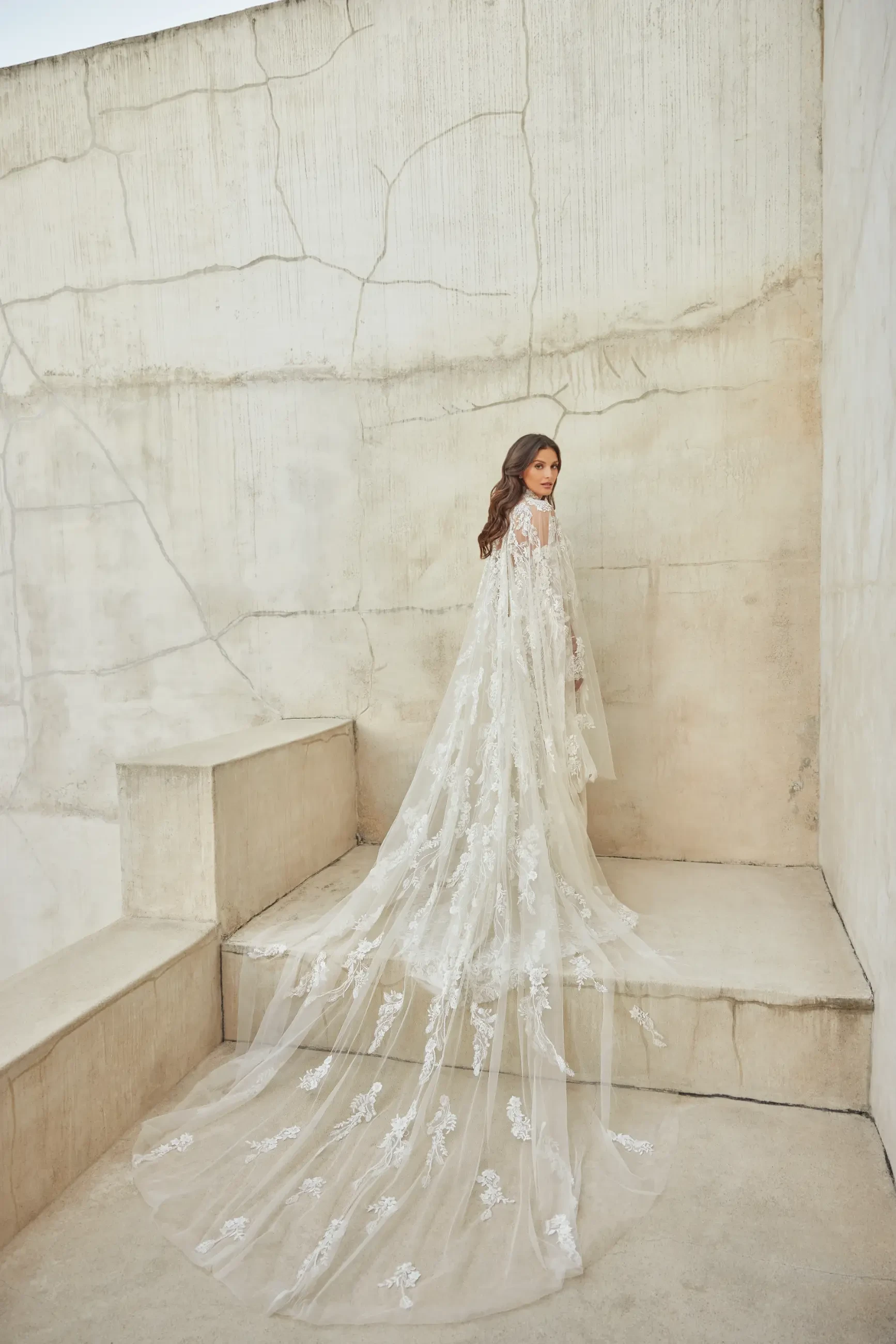 Model is wearing the Lotus gown, a stone-colored strapless mermaid dress with hand-sewn lace appliques, beads, sequins, a sweetheart neckline, and a detachable beaded tulle cape.