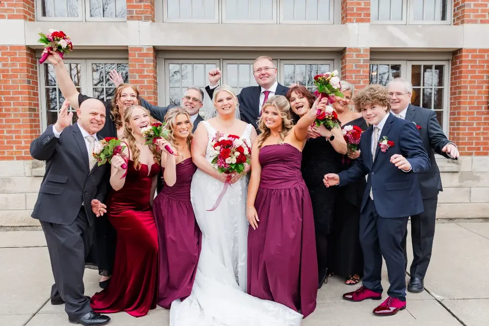A group of people in formal attire celebrating outdoors, holding bouquets and posing joyfully.