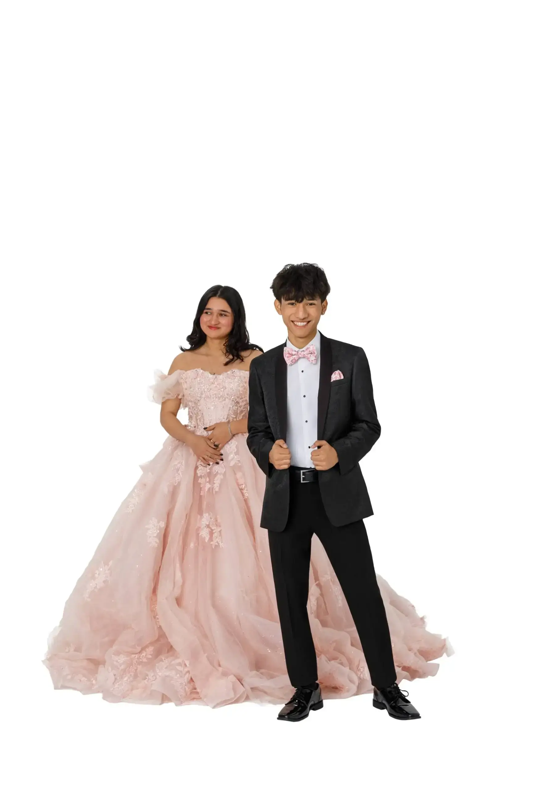 A girl in a pink gown and a boy in a black suit with a bow tie, standing together against a white background.