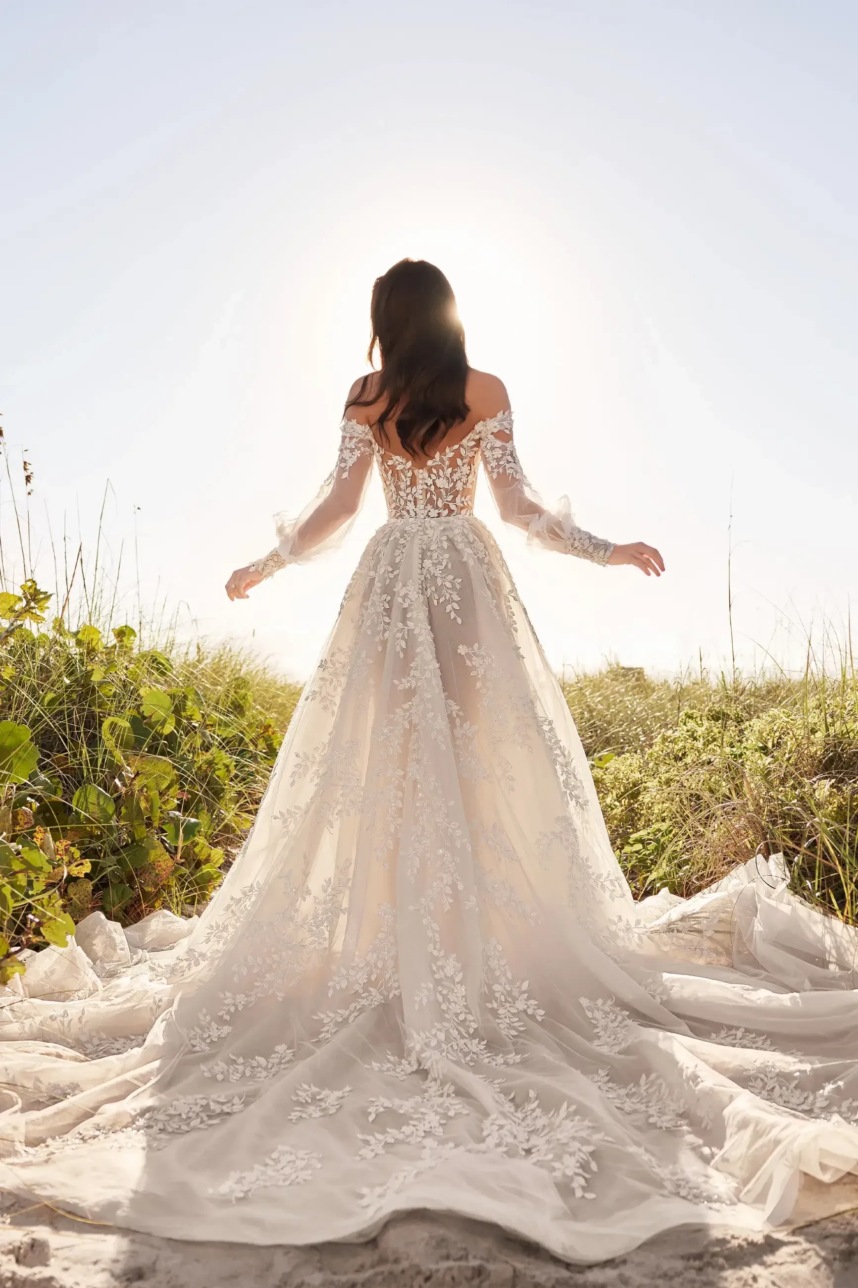 model is wearing an off the shoulder a-line wedding dress with a long train