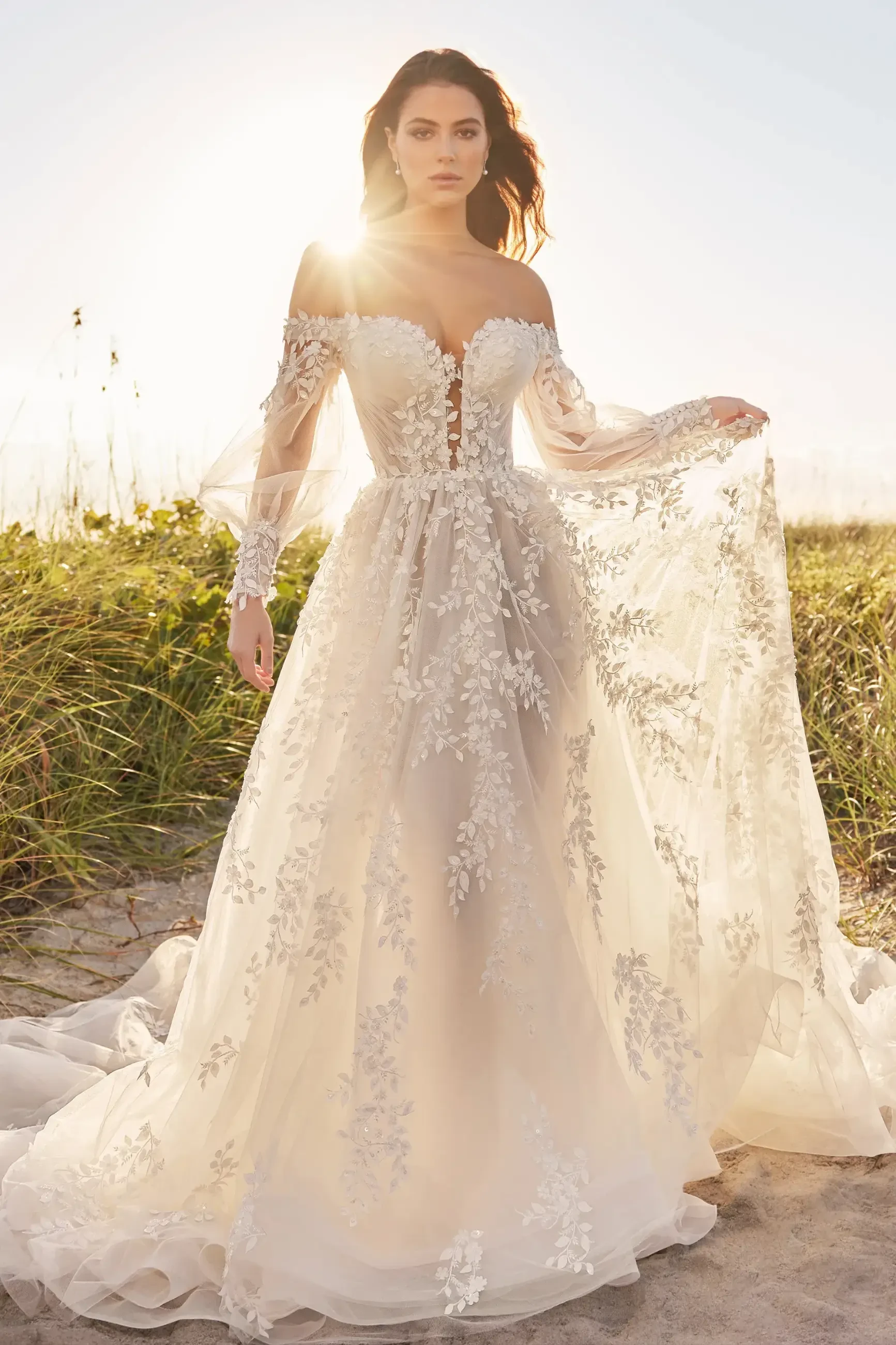 model is wearing an off the shoulder a-line wedding dress with a long train